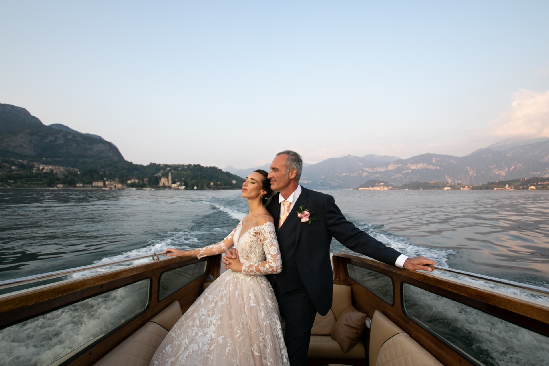 Newlyweds on a wooden boat surrounded by water and mountains, photographed by Sicily Wedding Company